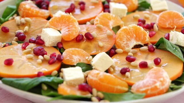 Close-up shot of the salad with persimmon, pomegranate, feta, spinat, orange and nuts.
