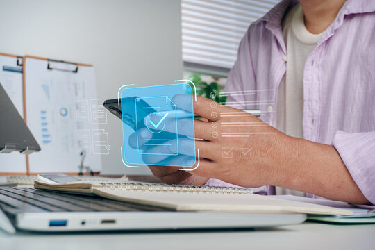 Person holding smartphone with digital document checklist and approved checkmark hologram icons, concept of mobile business application, online paperwork verification, and digital workflow management.