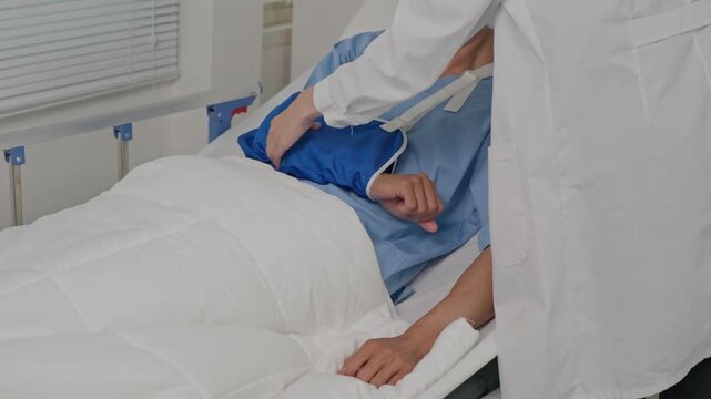 Nurse assisting patient with arm sling in hospital bed