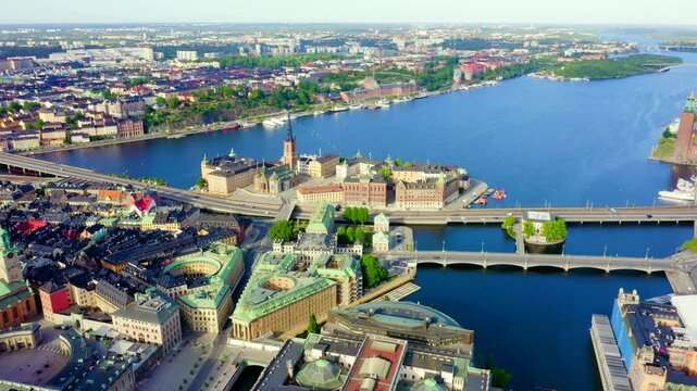 Stockholm, Sweden. Riddarholmen Church, its cast-iron spire rising above the island's historic palaces, aerial panoramic view over Lake Malaren and Gamla Stan under clear summer light. Drone footage