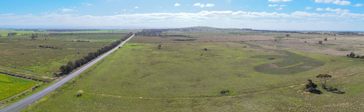 Panoramic aerial view of open farmland paddocks, a rural road&nbsp;and the low volcanic mound of Mount Cottrell, Victoria, Australia. Expansive green agricultural&nbsp;plains and undeveloped land