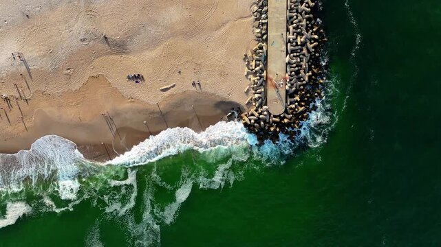 Top-down aerial of green ocean waves crashing on Jenks Beach with people, sunny day