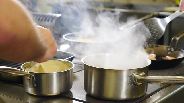 Close-up of chef hands placing and removing stainless steel pots on industrial gas stove. Hot steam rising from boiling sauces, professional restaurant kitchen atmosphere, dynamic cooking action 4k