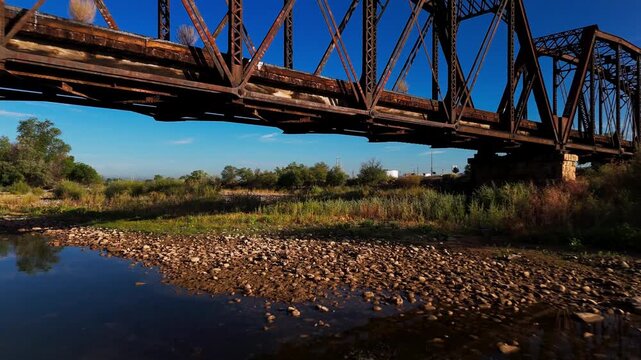 Flying beneath a train bridge near Grand Junction, Colorado. Then, a slow rise. Filmed mid morning in the late summer. Passes over the Colorado River. Near Colorado National Monunent.