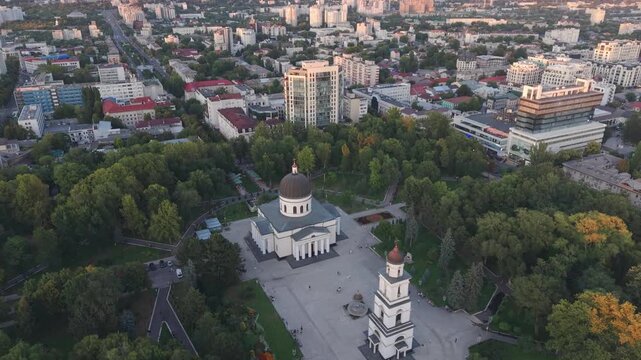 Aerial drone view of the Nativity Cathedral and its bell tower surrounded by Cathedral Park in central Chisinau, Moldova. Historic Orthodox architecture stands among green trees with the modern capita