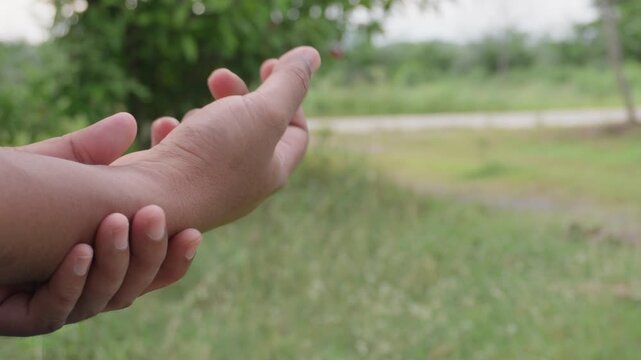 Close-up of person massaging hand and wrist with fingers in natural green garden background, concept of hand care, body relaxation, spa therapy, physical wellness, and joint pain relief.