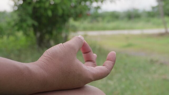 Person hand in meditation yoga mudra gesture resting on knee with scenic green nature trees bokeh background, concept of mindfulness, mental health relaxation, and inner peace.