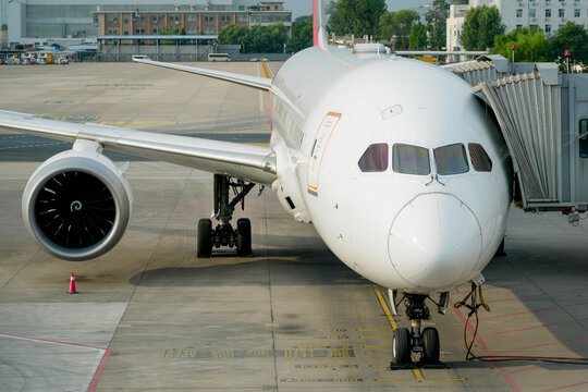 Front view of the cockpit and fuselage and wing of the aircraft with the engine at the jet bridge and apron