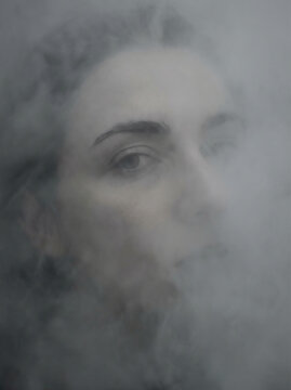 Close‑up of woman&rsquo;s face partially hidden by mist, soft monochrome tones creating mysterious and ethereal portrait.