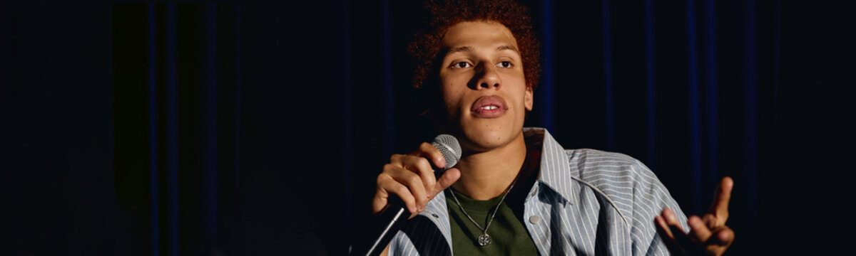 Young adult male student performing on theater stage holding microphone and gesturing. Image suitable for promoting drama classes, public speaking workshops, and youth arts programs