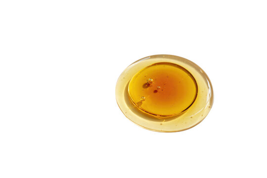 A circular puddle of dark golden honey or amber syrup isolated on a black background, with visible air, bubbles and a, smooth reflective surface