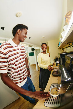 Vertical image of young African American man and woman smiling while making coffee in office kitchen, representing workplace wellness and employee benefits