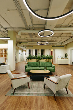 Vertical image of modern open plan office lounge area featuring green sofa and armchairs, representing contemporary workplace design suitable for corporate real estate marketing