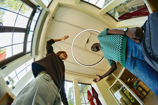 Young adult Caucasian man and young adult Black man greeting each other with high five in modern office lobby, representing diverse teamwork and corporate partnership, low angle shot