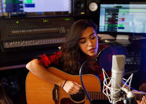 Young female singer with acoustic guitar recording a song promo in a studio