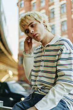Caucasian Gen Z man sitting outdoors, listening to music with wired earphones. Image suitable for youth lifestyle marketing and digital technology campaigns, vertical