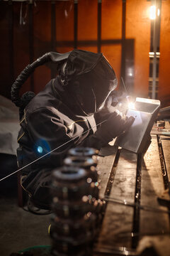 Vertical image of professional welder in protective gear welding metal parts at workbench. Image suitable for industrial manufacturing and vocational training promotions