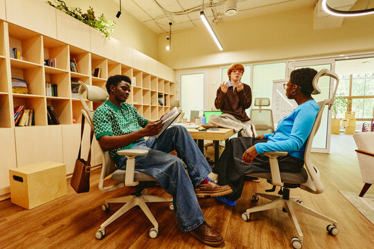 Diverse young adult colleagues collaborating in modern office, discussing project details. Image suitable for corporate communication and remote work hybrid team marketing campaigns