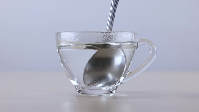Stirring Clear Liquid in Glass Cup with Metal Spoon