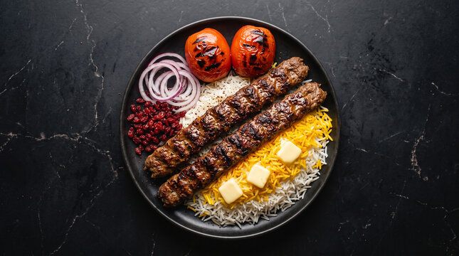 Top down view of chelo kabab plate with saffron rice, butter cubes, grilled tomato and barberries