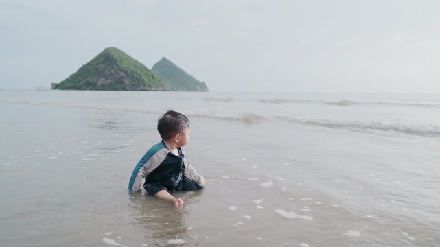 Cute Toddler Playing in Sea Water on the Beach with Mountain Background
