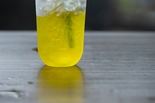 Iced yellow chrysanthemum tea in a plastic cup on a wooden table.A close-up shot capturing the bottom half of a clear takeaway plastic cup filled with an iced vibrant yellow beverage