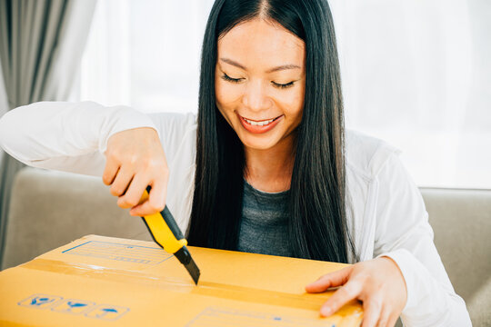A woman uses a utility cutter for precision unboxing revealing contents of a shopping cardboard box. Engaged in opening unpacking and surprise from online shopping. Business and retail concept.