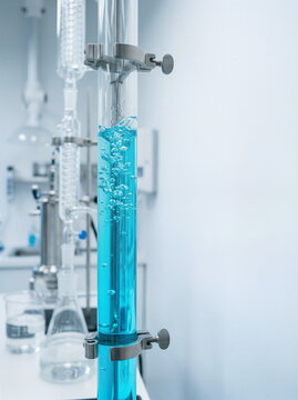 Glass column with bubbling blue liquid, part of chemical experiment in modern laboratory, representing scientific discovery and innovation.