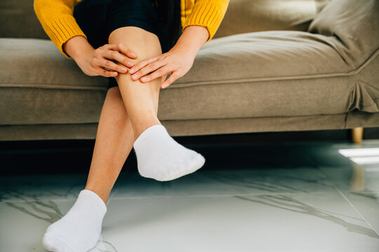 A woman seated on a sofa holds her painful ankle in close-up depicting discomfort. Illustrating health care varicose vein prevention and emphasizing leg recovery and pain relief.