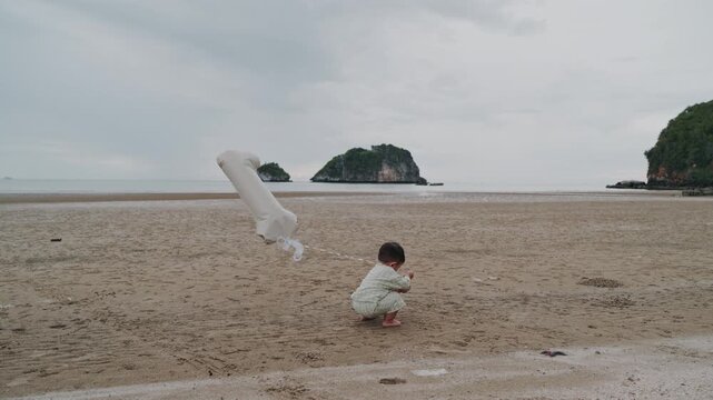 Cute toddler standing on sandy beach holding number one balloon for birthday party