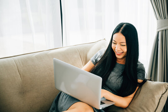 Happy woman on sofa uses laptop for ecommerce learning watching videos. Embracing studying success and relaxation at home. Modern technology for education and shopping.