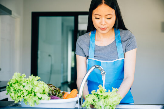 Cheerful woman prepares fresh vegetables for a salad washing them in the kitchen sink. Highlighting hygiene and a passion for clean eating in her vegetarian lifestyle at home.