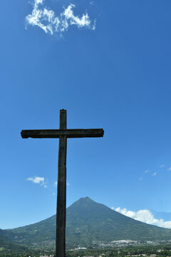 Cruz de piedra con vista hacia el cielo azul y volc&aacute;n de agua en Antigua Guatemala.