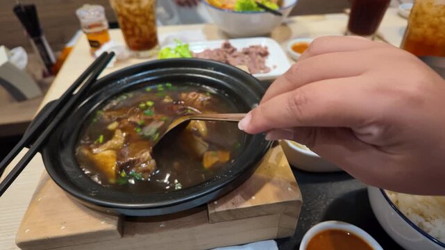 Person Eating Thai Beef Soup in Clay Pot at Bangkok Restaurant