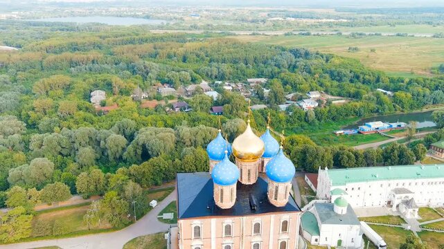 Ryazan, Russia. The Assumption Cathedral, its five blue and gold domes rising above the Kremlin hill, aerial panoramic view over the Oka River valley. Drone footage, Departure of the camera