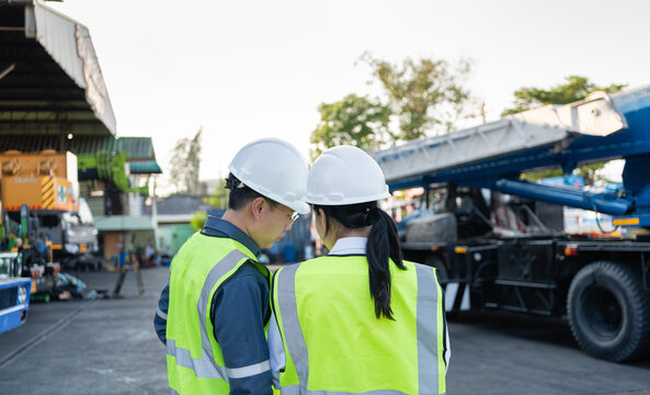 Rear view crane inspection features two engineers wearing white hard hats discussing outdoor heavy machinery maintenance