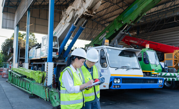 Midshot of lifting operations safety shows two engineers, male and female, in hardhats writing on a clipboard near mobile cranes