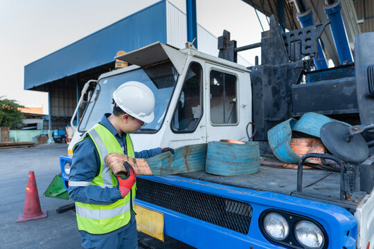 Midshot of crane preventive maintenance depicts a male worker wearing a helmet carefully inspecting orange lifting slings