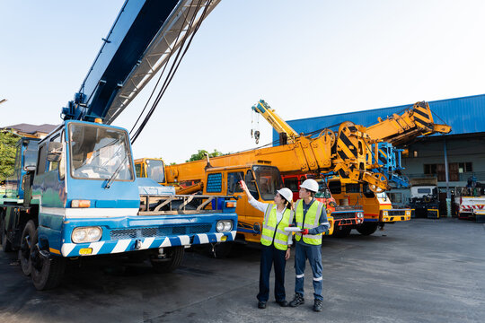 At a lifting equipment yard, an inspection involves male and female engineers assessing the crane boom holding a clipboard