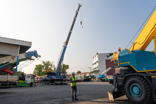 Mobile crane boom undergoes preventive maintenance while two helmeted engineers holding a tablet and clipboard perform outdoor inspections