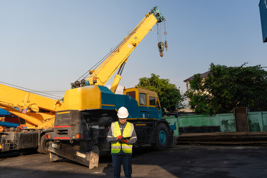 Boom of lifting equipment undergoes inspection while a male technician in a hard hat records safety data on his tablet