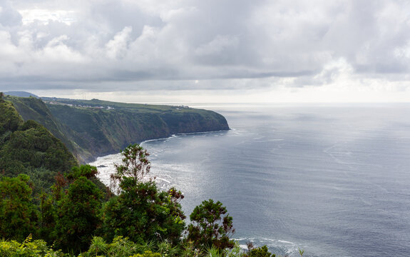Coastal cliffs, Sao Miguel. Green vegetation borders the Atlantic Ocean beneath layered clouds in Nordeste, Portugal.
