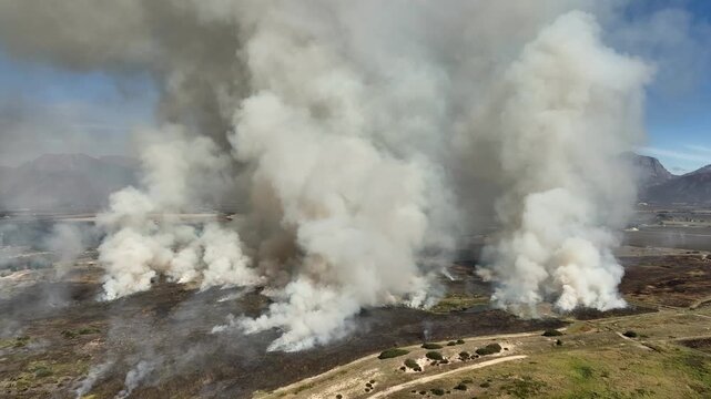 Aerial circles grass fire on mtn plateau filling sky with thick smoke