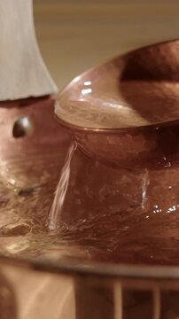 Fresh water scooped up with copper ladle from copper sauna bucket vertical.