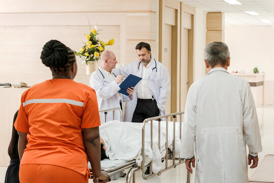 Doctors and a nurse in a hospital corridor wheel a patient on a stretcher while discussing notes, coordinating urgent care.