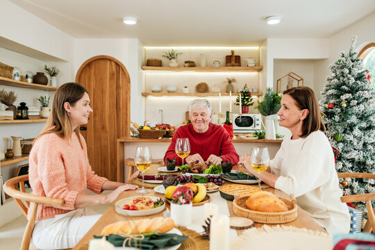 Happy multigenerational family enjoying Christmas dinner together at a festive table, sharing delicious food and conversation in a cozy home filled with warm holiday cheer and joy.