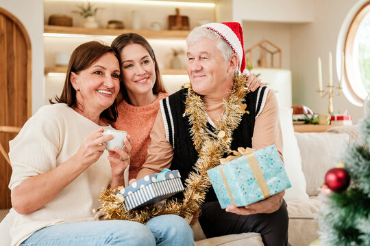 Happy multigenerational family sitting together with Christmas gifts at home, smiling and embracing while enjoying a warm, joyful holiday celebration filled with love and togetherness.