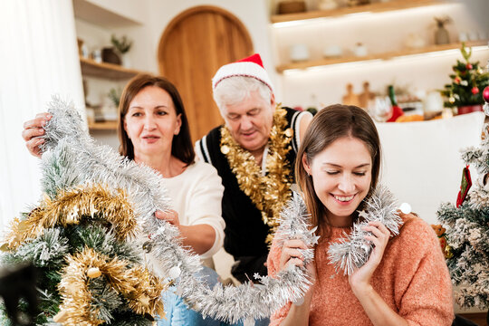 Happy multigenerational family decorating a Christmas tree with sparkling tinsel at home, smiling and sharing a joyful moment together while enjoying a warm festive holiday tradition.