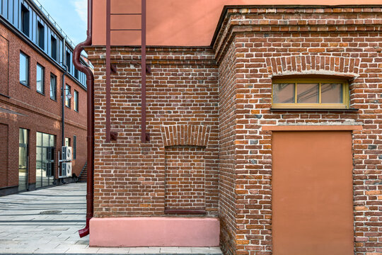 old industrial building after renovation works. red brick wall with downspout and fire escape.