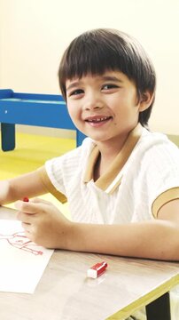Smiling young boy drawing with a red marker at a table in a bright classroom or playroom